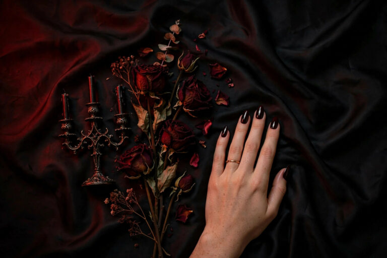 Goth vamp nails with glossy black cherry polish on almond nails styled with dried roses