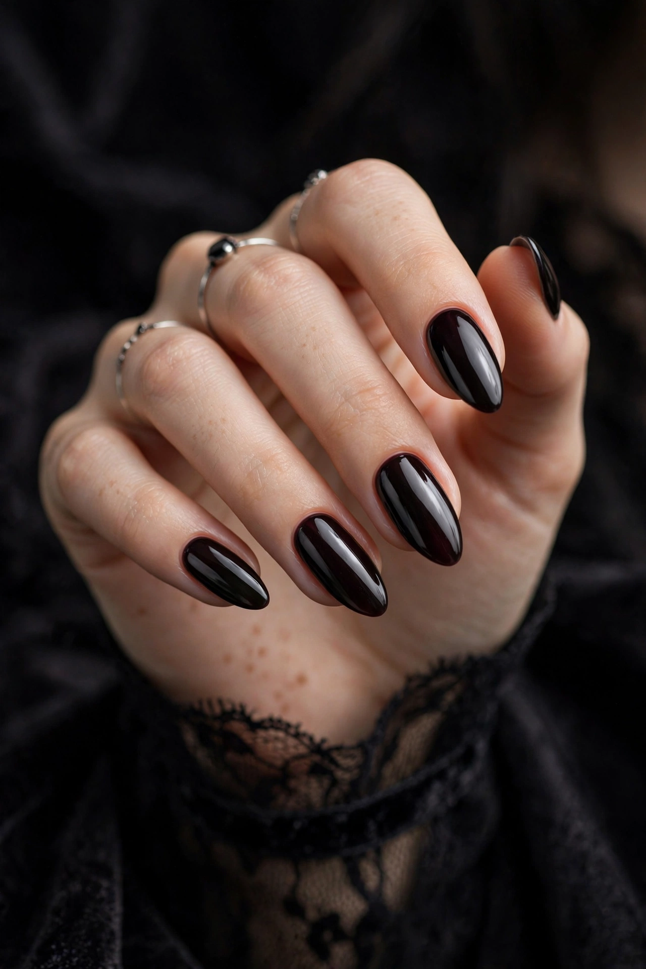 Goth nails with glossy black cherry polish on almond-shaped nails styled with dried roses